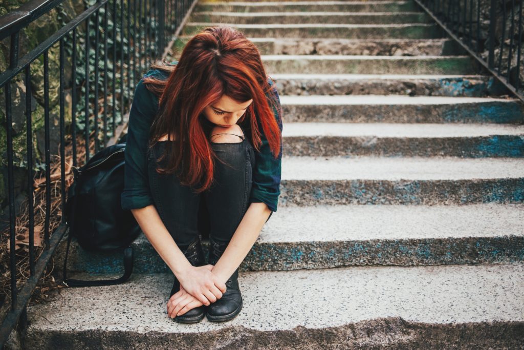 Depressed young woman sitting on stairs outdoors